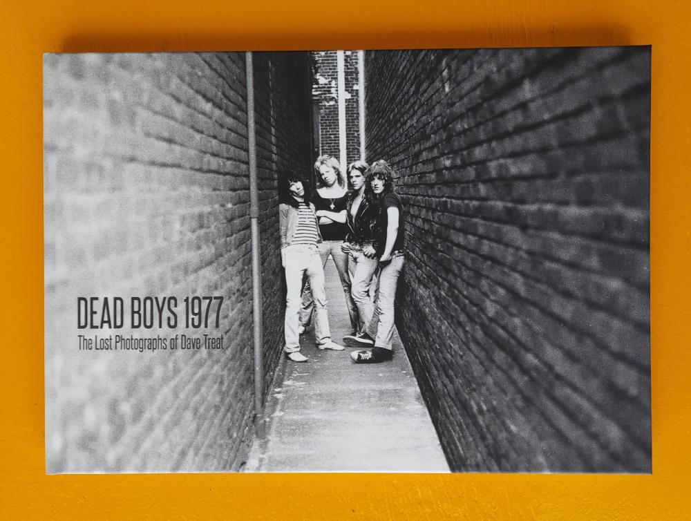 a black and white photograph of four boys with long hair/mullets standing in an alley