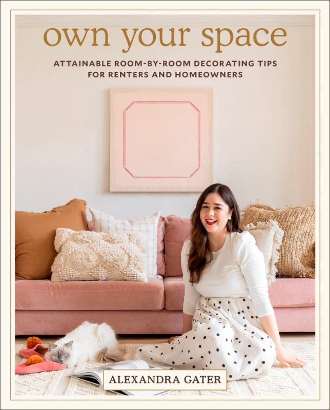 The author, a woman with long brunette hair, seated on the floor in front of a pink couch with a eclectic selection of throw pillows