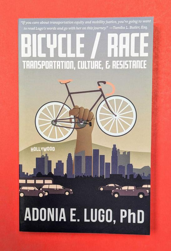 bicycle race book cover featuring a fist holding a bicycle above the LA skyline