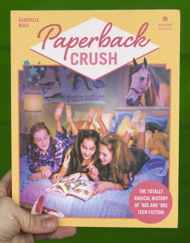 Three young women laying on a bed, flipping through a book.