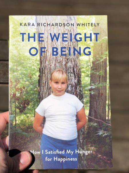 A young girl standing with her back to a tree, smiling at the camera.