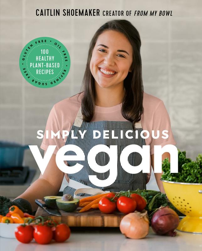 a woman with brown hair standing behind a spread of delicious looking fruits and veggies